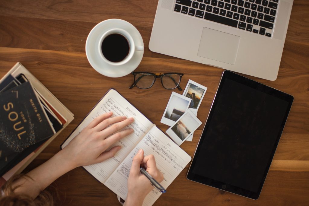 A person writing in a notebook on top of a wooden table.